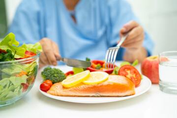 Asian elderly woman patient eating salmon steak breakfast with vegetable healthy food in hospital.