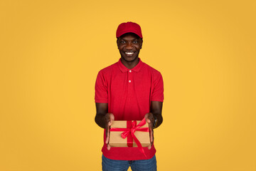 Happy millennial african american guy courier in uniform gives box gift