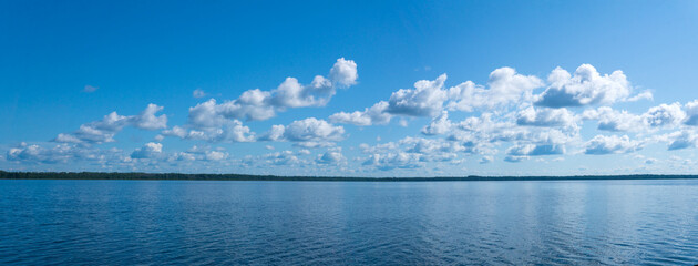 natural landscape, waterscape, panorama overlooking a large lake under a blue sky with clouds and a distant wooded shore