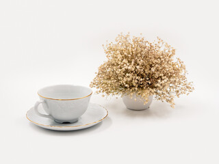 Obraz na płótnie Canvas Composition of white porcelain for tea drinking on a light white background with a delicate bouquet of dried flowers.