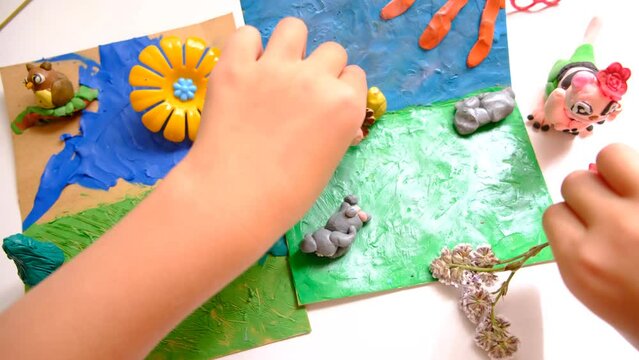 Child smearing colorful plasticine on cardboard and creating fairy tale card with cartoon animals, using nature details, dry flowers, cone, leaves
