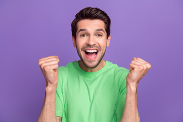 Photo of impressed astonished man with stubble dressed green t-shirt raising fists win betting isolated on purple color background