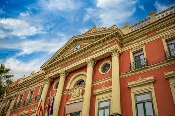 Fototapeta na wymiar Facade of the Town Hall of Murcia, Spain with salmon colours, columns and blue sky.