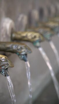 Closeup, ancient taps made in bronze, pouring water in the fountain.