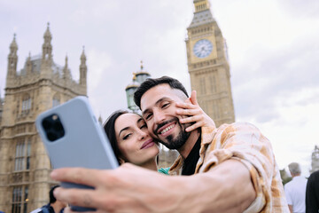 Young couple taking selfie together in front of Big Ben clocktower in London