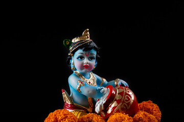Hindu god Krishna. Statue with flowers on a black background