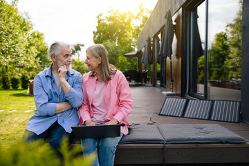 Man and woman sitting on house porch with solar panel using notebook.
