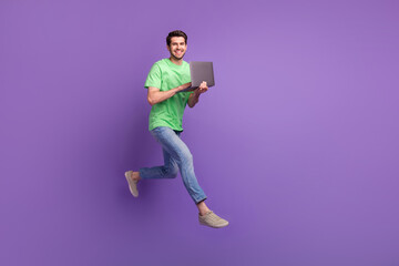 Fototapeta na wymiar Full length body photo of young funny positive man jumping running fast netbook user fast delivery ad isolated on violet color background