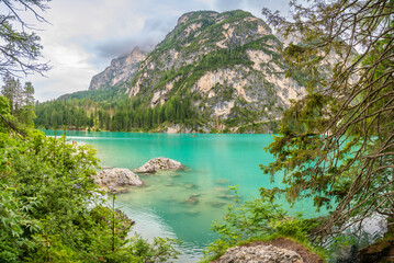 Braies lake surrounded by pine forests and the rocky ranges of the Dolomites in cloudy day, Italy.