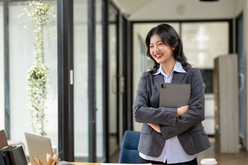 Smart and self confident businesswoman standing with tablet in hand at table in office.