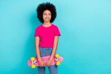 Photo of cheerful satisfied girl with afro chevelure wear pink t-shirt hold skateboard look empty space isolated on blue color background © deagreez