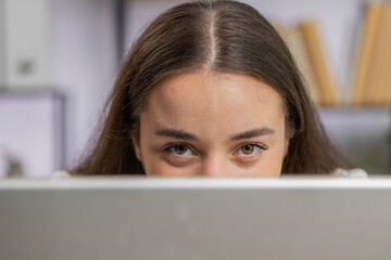 Confident business woman hiding behind laptop computer, looking at camera, spying his colleagues...