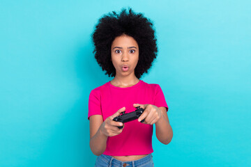 Portrait of excited astonished focused schoolgirl dressed stylish t-shirt hold playstation joystick isolated on blue color background © deagreez