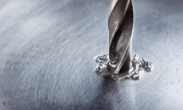 metal drill bit with lubrication oil liquid make holes in steel billet on industrial drilling machine. Metal work industry