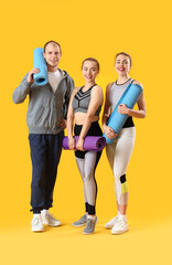 Fototapeta premium Sporty young people with fitness mats on yellow background