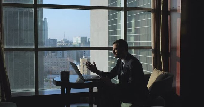 Side view of annoyed company boss having video call on laptop and scolding colleagues for bad work performance. Furious man yelling and emotionally gesturing hands.