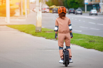 Woman in protective gear riding electric unicycle, monocycle or mono wheel. Trendy woman in helmet on electric vehicle, view from back. Woman ride electric mono wheel, personal electric transport