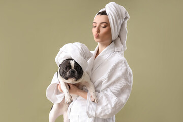 Young woman with her French bulldog in towels on green background