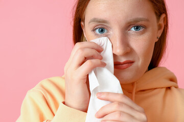 Allergic young woman with tissue on pink background, closeup