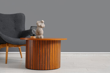 Cozy armchair and wooden coffee table with woman figurine near grey wall