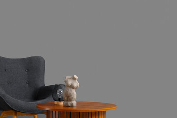 Cozy armchair and wooden coffee table with woman figurine near grey wall
