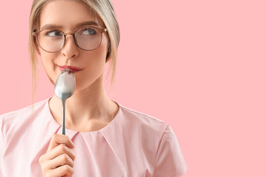 Thoughtful young woman with spoon on pink background, closeup