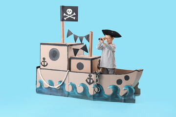 Cute little pirate with spyglass in cardboard ship on blue background