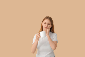 Young woman with sensitive teeth and cup of hot coffee on beige background