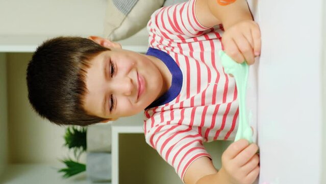 A six-year-old boy plays with slime while sitting at a table at home. A toy for the development of fine motor skills and creativity in children