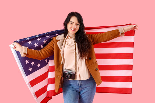 Beautiful young female tourist with USA flag on pink background