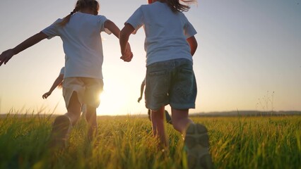 a group of children run across the field on the grass. happy family kid lifestyle dream concept. children running in a field with tall grass on the sunset. girls holding hands in the foreground