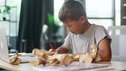Portrait of exhausted school boy with failed crumped papers while writing in notebook at home Tired little kid child with creative block or lack of inspiration indoors Stress education concept