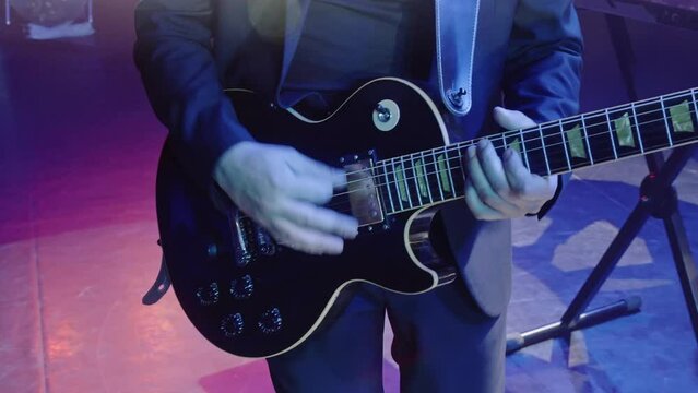 Handheld shot of guiatarist performing on stage. Close-up of male artist playing instrument at night show event. He is enjoying rock music during the concert. 