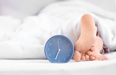 Sleeping woman's feet with alarm clock in bed, closeup