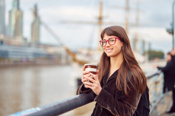 portrait beautiful young caucasian student woman holding a cup of coffee outdoors smiling