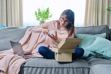 Mature woman sitting at home unpacking cardboard box with online shopping