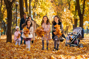 portrait of big family in autumn city park, children running with armful of leaves, happy people playing together and scattering yellow leaves, beautiful nature, bright sunny day