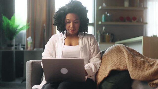Pretty young woman freelancer working online typing browsing on laptop laying on sofa at late evening indoors Positive female enjoying great working day at cozy home