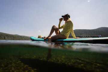 A young woman cools off in an alpine lake at the base of Mt. Hood with her standup paddle board on a summer day. 