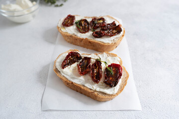 Two toasts with cottage cheese, sun-dried tomatoes and thyme sprigs on a white background. Breakfast, snack.