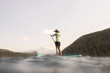 A young woman cools off in an alpine lake at the base of Mt. Hood with her standup paddle board on...