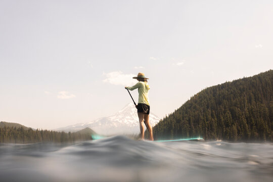 A young woman cools off in an alpine lake at the base of Mt. Hood with her standup paddle board on a summer day. - Powered by Adobe
