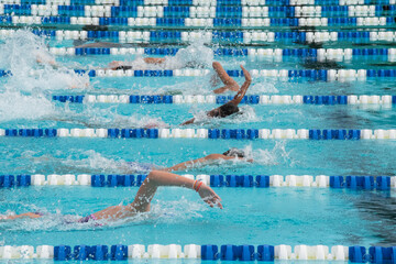 Multiple people swimming laps in the lanes of an outdoor swimming pool