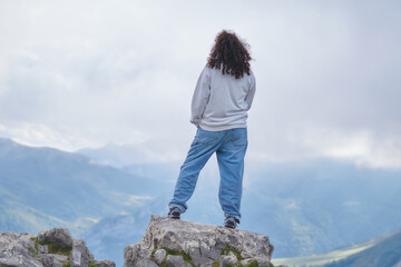 Woman in Jeans on Mountain Peak Overlooking Majestic Cloud-Cloaked Range
