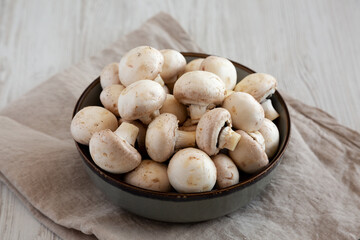 Raw White Champignon Mushrooms in a Bowl on a white wooden background, side view.