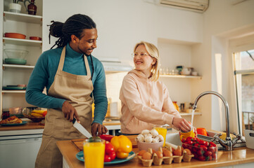 A happy multicultural couple is preparing a healthy homemade meal while standing in a kitchen at home.
