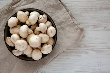 Raw White Champignon Mushrooms in a Bowl on a white wooden background, top view.