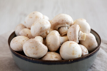 Raw White Champignon Mushrooms in a Bowl on a white wooden background, side view. Close-up.