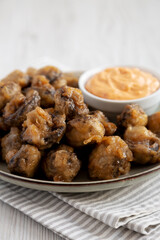Homemade Crispy Deep Fried Mushrooms with Spicy Mayo on a Plate on a white wooden background, side view.
