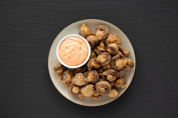 Homemade Crispy Deep Fried Mushrooms with Spicy Mayo on a Plate on a black background, top view.